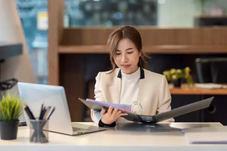 beautiful young asian businesswoman holding documents checking authenticity laptop is placed office table Web H